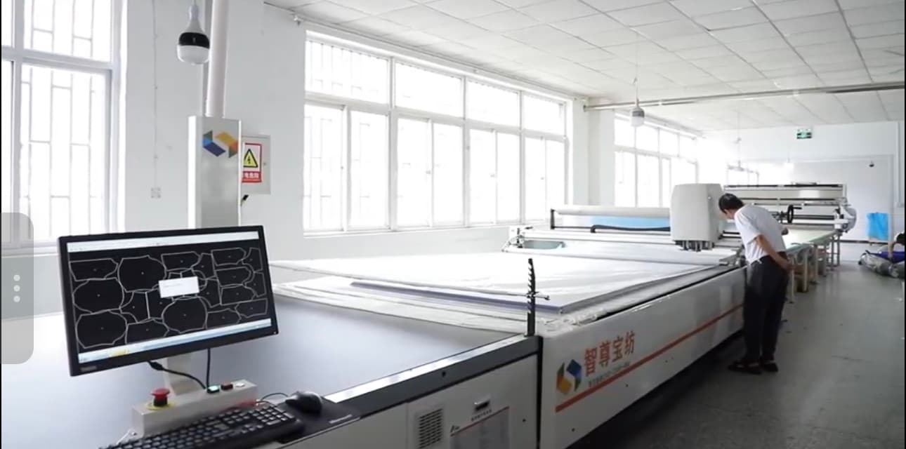 Technician operating a computer-controlled cutting table with nested pattern pieces on screen